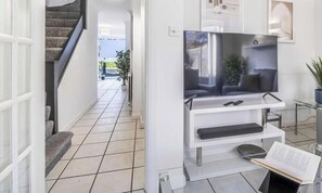 A modern living room with a flat-screen TV on a white stand, a staircase, and a view of the outdoors. - Angus Suites is a modern 4 bedroom house near Peterborough City Centre. Includes free WiFi, Smart TV, a fully equipped kitchen, private garden, and free parking. Situated in a quiet residential area with open field views. (Peterborough)