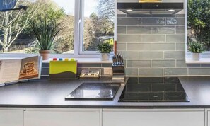 A modern kitchen with a built-in stove, a window with a view of trees, and a potted plant on the counter. - Angus Suites is a modern 4 bedroom house near Peterborough City Centre. Includes free WiFi, Smart TV, a fully equipped kitchen, private garden, and free parking. Situated in a quiet residential area with open field views. (Peterborough)