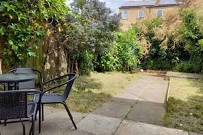 Une terrasse avec une table et des chaises, un chemin de pierres et, au fond, un bâtiment en briques.