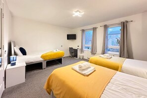 A hotel room with two beds, a desk, a chair, a TV, and windows with curtains. - Clayton House Contractors Accommodation | 6BR House Peterborough (Peterborough)