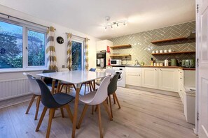 A modern kitchen with a dining table, chairs, a microwave, and a washing machine. - Clayton House Contractors Accommodation | 6BR House Peterborough (Peterborough)