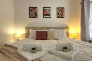 Una habitación de hotel con una cama, dos lámparas de noche, tres cuadros enmarcados y dos toallas con botellas encima.