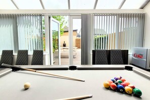 A pool table with balls and cues, a Diet Coke cooler, and a view of the outdoors through large windows.
