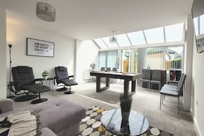A modern living room with a pool table, comfortable seating, and large windows.