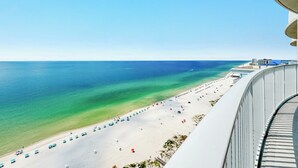 Vista a la playa desde un balcón, con cielo despejado, arena y algunas sombrillas.