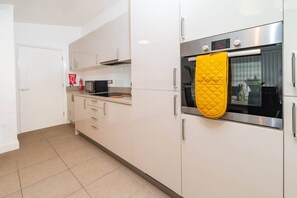 A modern kitchen with white cabinets, a microwave, an oven, and a yellow oven mitt hanging on the oven door. - Discover our modern 2-bed apartment in historic Old Town Huntingdon. Features a fun pool/table tennis table, dedicated workspace, and a fully equipped kitchen. Includes a free, pre-registered parking. A unique retreat for work or leisure! (Cambridgeshire)