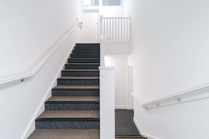 A staircase with carpeted steps, white walls, and a white railing.