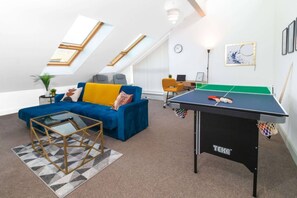 Un salon moderne avec un canapé bleu, une table de ping-pong et une table basse en verre.