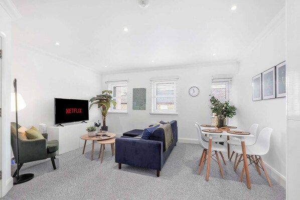 A modern living room with a flat-screen TV, a sofa, a dining table, and a potted plant.