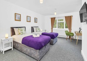 A hotel room with two beds, a desk with a chair, a TV, and a window with curtains.