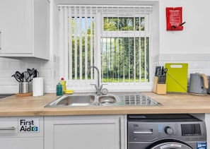 Une cuisine équipée d’un évier, de stores aux fenêtres, d’une couverture anti-feu et d’un lave-linge.