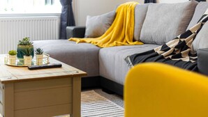 A living room with a sofa, a yellow chair, a coffee table with plants and a remote control, and a striped rug. - The No.7 | Modern 3BR House | Pool Table Pingpong (Brampton)