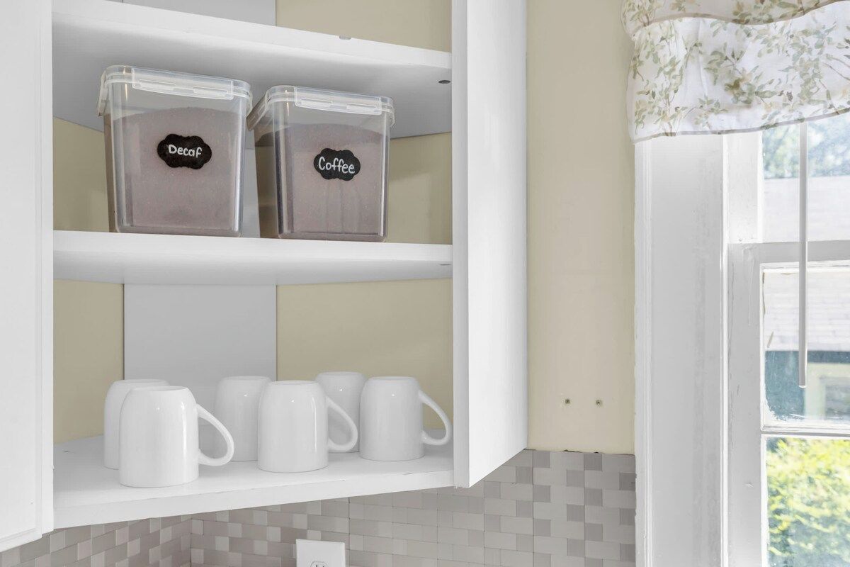 A kitchen with white cabinets, two labeled containers, and white mugs on the shelf.