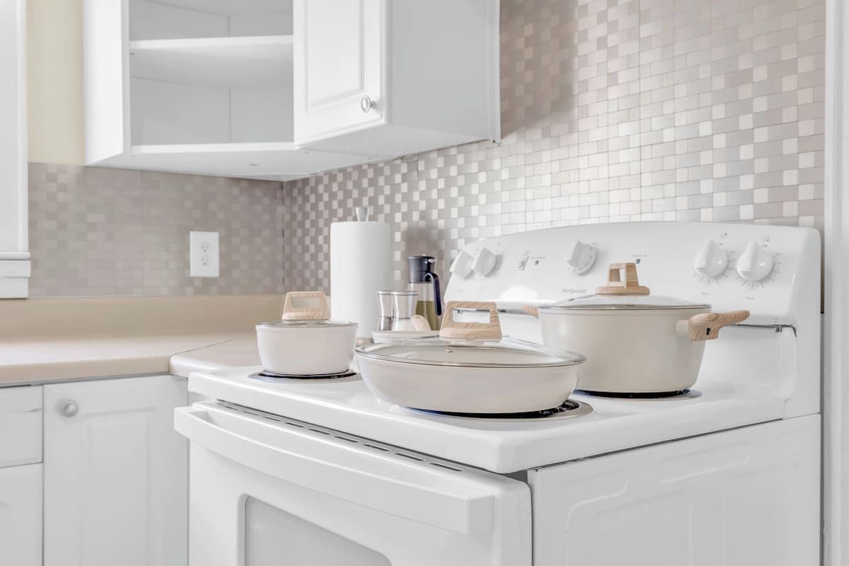 A kitchen with white cabinets, a tiled backsplash, and a stove with pots and pans.