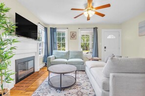 A living room with a fireplace, a ceiling fan, and a sofa. - Cute Bungalow near Downtown, Sleeps 6 (Spartanburg)