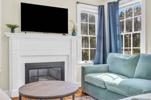 Una sala de estar con chimenea, un televisor de pantalla plana montado sobre ella, un sofá azul claro y una mesa redonda de madera.