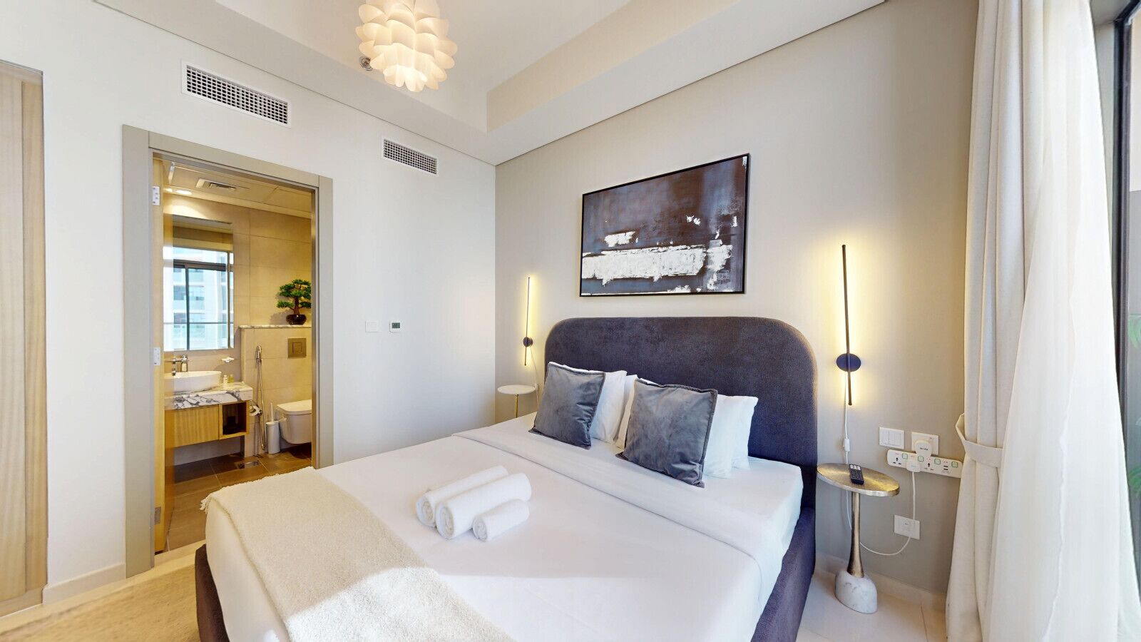 Et moderne hotelværelse med en stor seng, et natbord, et billede på væggen og et badeværelse, der kan ses gennem en åben dør.