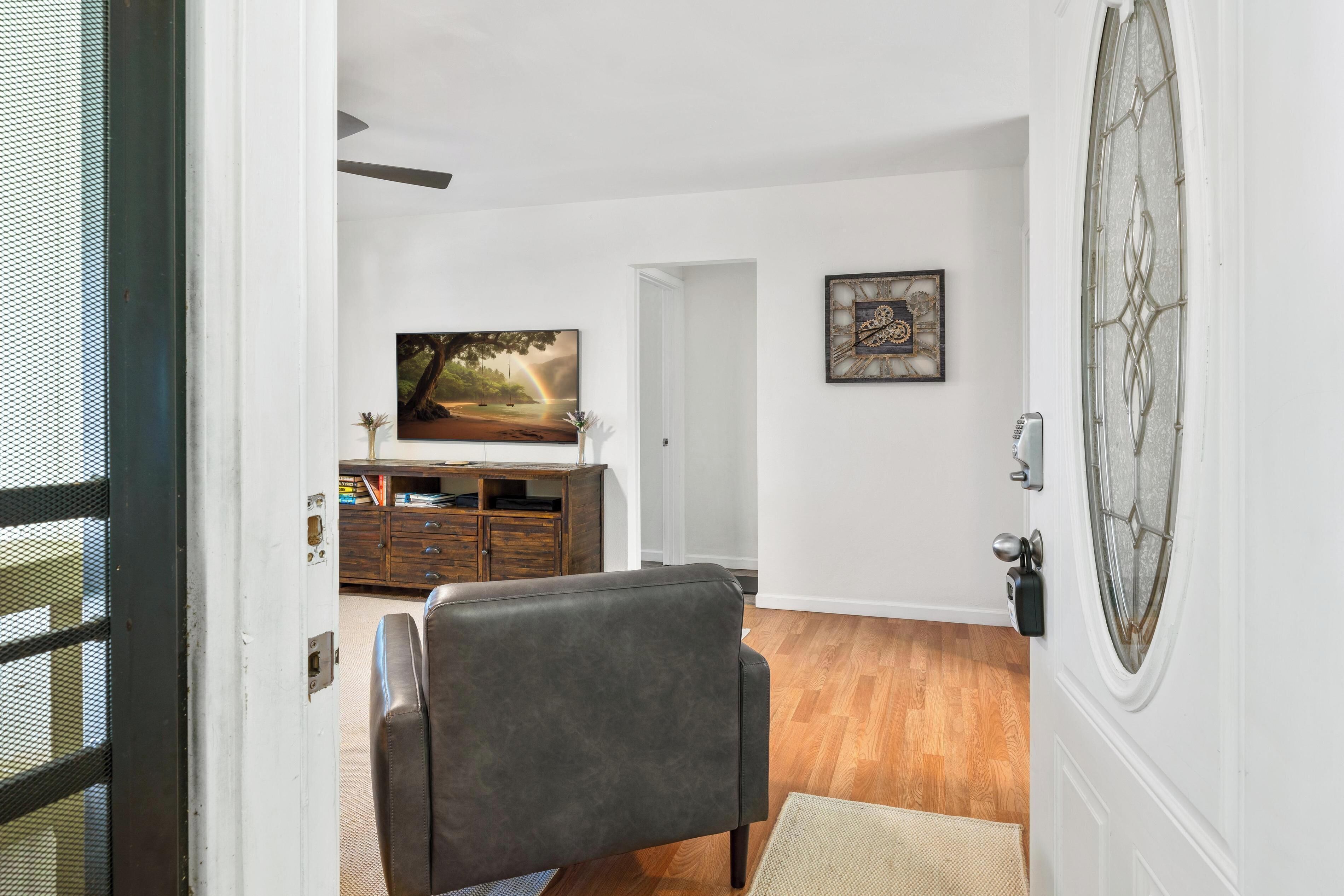 Sala de estar con sofá de cuero, un mueble de madera, un cuadro enmarcado y una puerta con panel de vidrio decorativo.