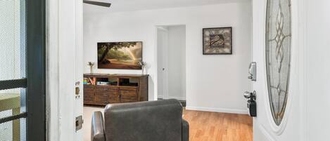 Sala de estar con sofá de cuero, un mueble de madera, un cuadro enmarcado y una puerta con panel de vidrio decorativo.