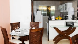 A compact kitchen with a glass dining table and wooden chairs, a refrigerator, a coffee maker, and a toaster. - Pousada Morro do Pico (Fernando de Noronha)