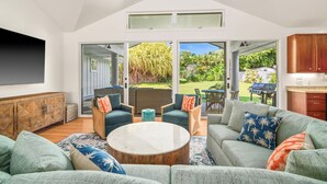 Un vaste espace de vie comprenant un grand canapé, une table basse et une table à manger avec des chaises. Il y a également une cuisine équipée de meubles en bois et d’une grande fenêtre donnant sur un jardin.