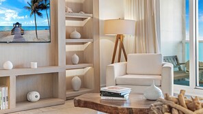 A modern living room with a beach view, a wooden bookshelf, a white armchair, and a lamp. - Luxury Vacation Rentals at 1 Hotel & Homes by LRMB (Miami Beach)