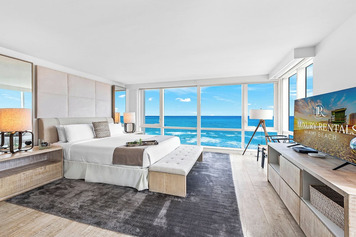 A modern hotel room with a large bed, a desk, and a view of the ocean.