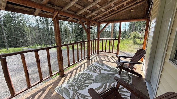 Una terraza de madera con vistas a un bosque, una silla y una mesa con un tapete estampado con hojas.