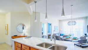 A modern kitchen with a large island, stainless steel sink, and pendant lighting.