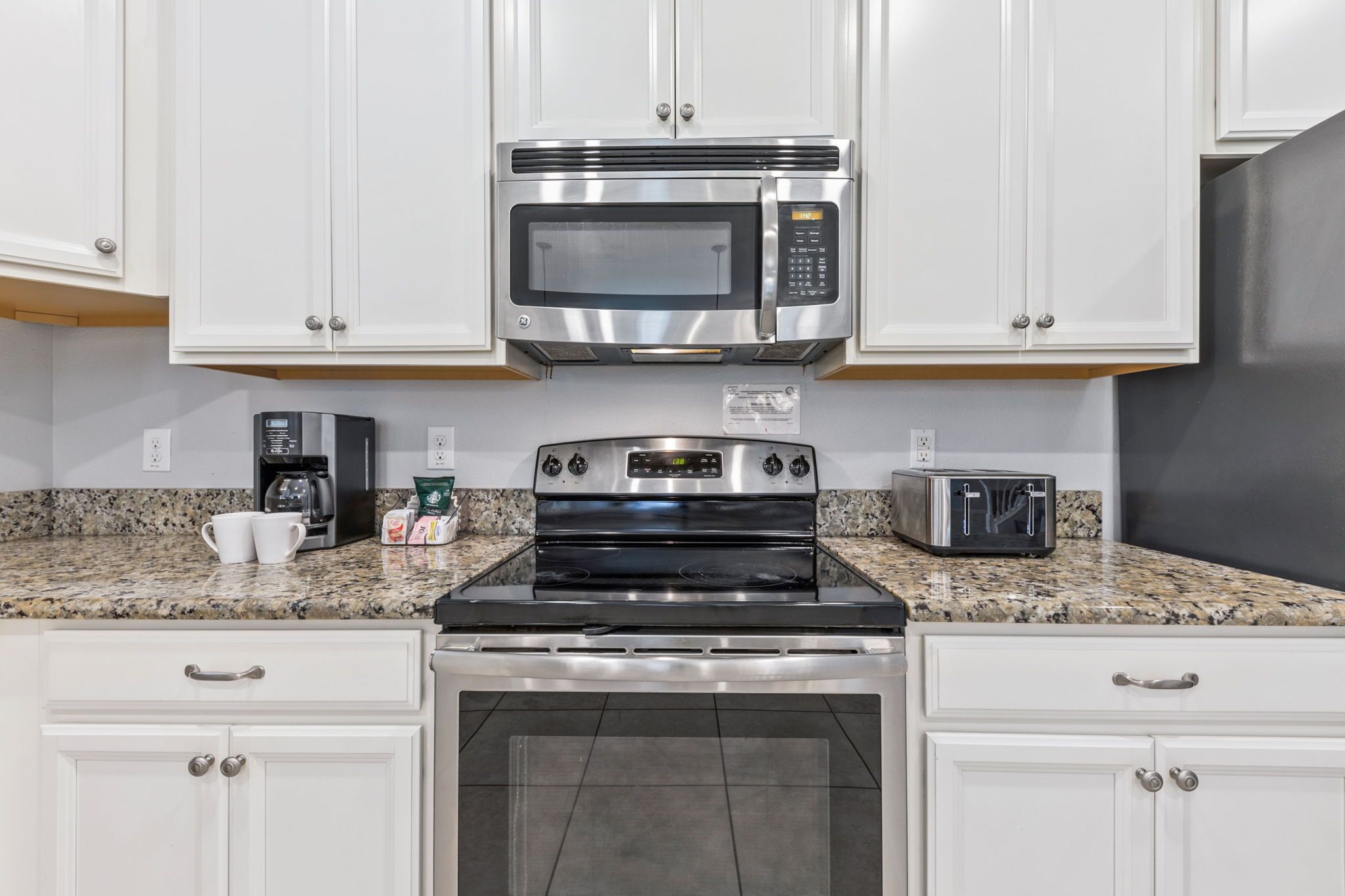 A kitchen with white cabinets, a stainless steel microwave, a stove, a toaster, and a coffee maker.