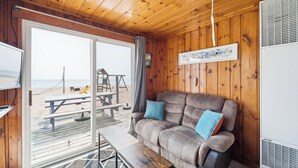 Eine Hütte mit Holzinnenraum, einem Sofa mit blauen Kissen, einem Holztisch und Blick auf den Strand durch eine Schiebetür.