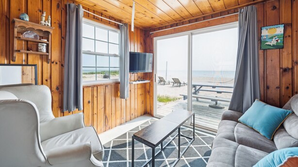Ein Holzinterieur mit einer Couch, einem Fernseher und Blick auf den Strand.