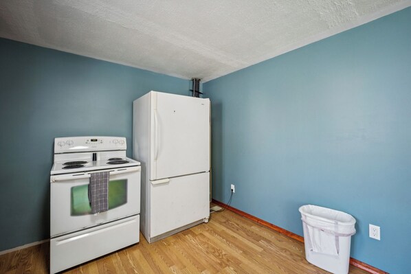 A kitchen with a white stove, oven, and refrigerator, wooden flooring, and a blue wall. - Barefoot Beach Resort (Oscoda)