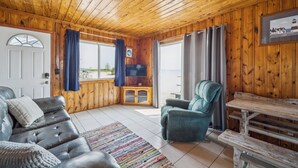 Ein gemütliches Blockhaus-Interieur mit Holzbalkendecke, einem Ledersofa, einem türkisfarbenen Sessel und einem Holztisch.