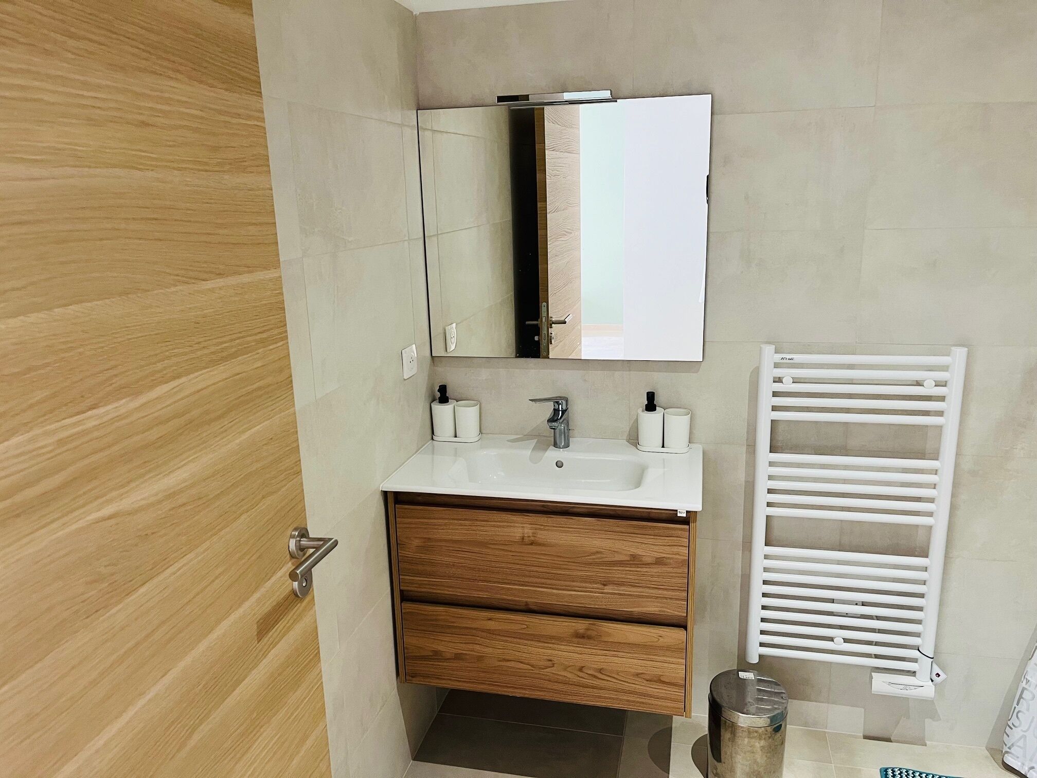 Un baño moderno con tocador de madera, lavamanos blanco, espejo y toallero blanco.