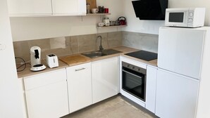 Une cuisine moderne avec des armoires blanches, un four encastré, un four à micro-ondes, un évier et une machine à café.