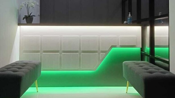 A reception area with a dark wall, a neon sign reading "Pondok Audy," and a green-lit reception desk. - Pondok Audy (Sinduadi)