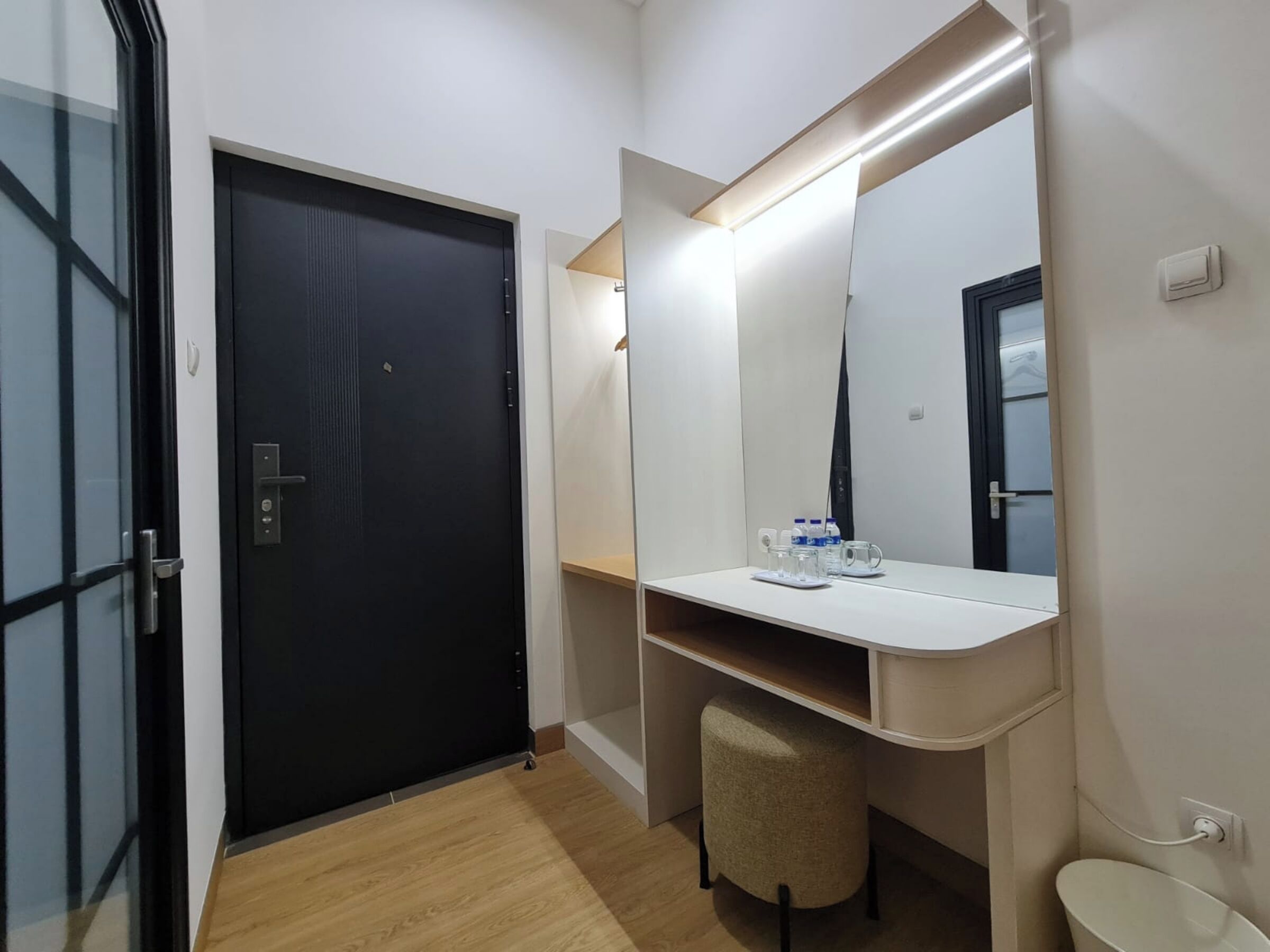 Une salle de bain moderne avec une porte noire, un meuble-lavabo blanc, un miroir et un petit tabouret.