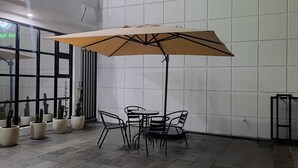 An indoor patio area with a round table and chairs, a large umbrella, and potted plants. - Pondok Audy (Sinduadi)