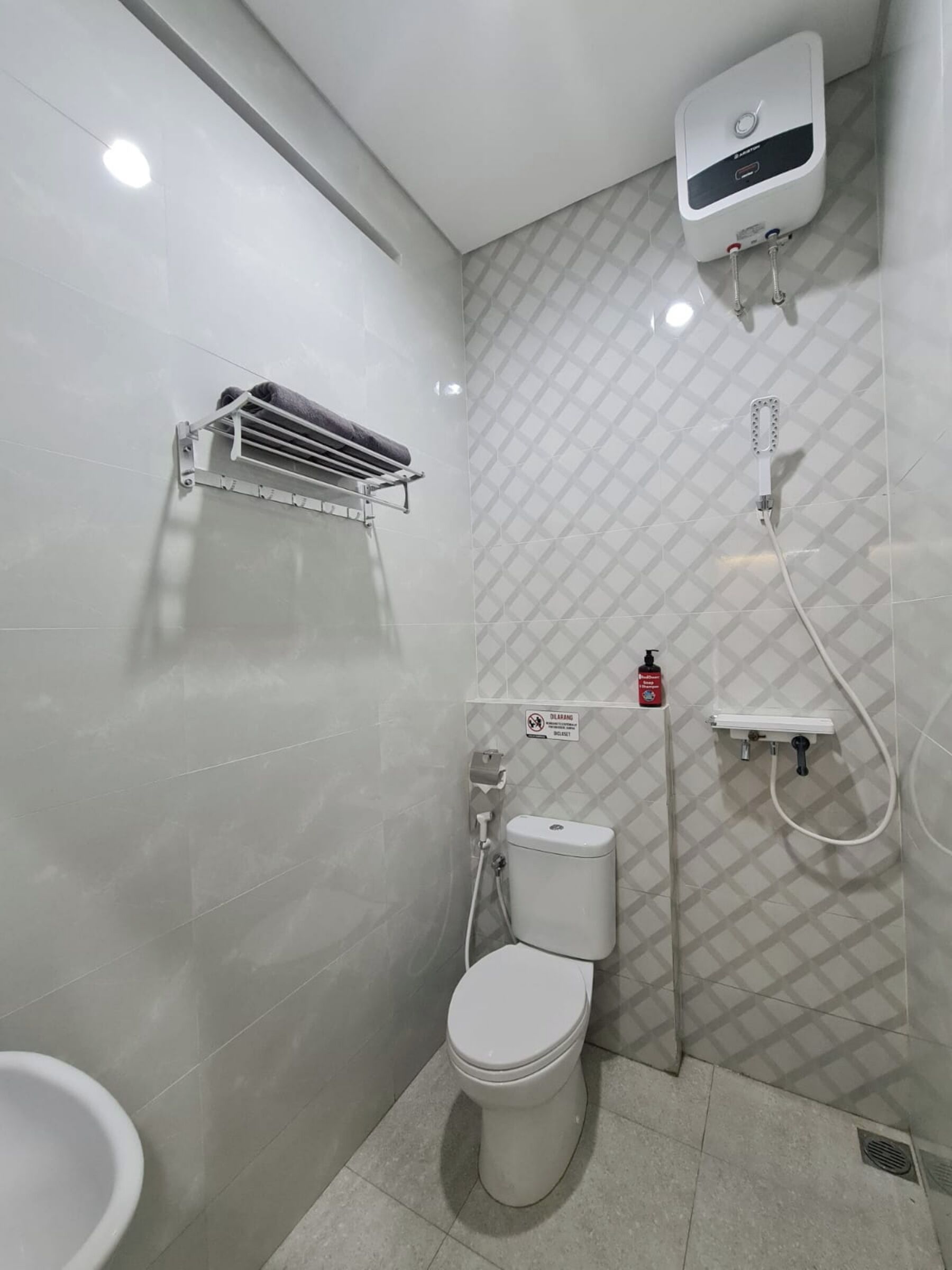 Casa de banho compacta com sanita, secador de mãos, chuveiro e dispensador de sabonete.