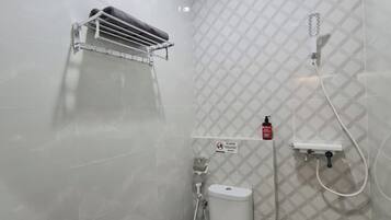 Casa de banho compacta com sanita, secador de mãos, chuveiro e dispensador de sabonete.