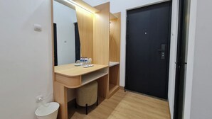 A modern bathroom with a wooden vanity, a mirror, a black door, and a white trash bin. - Pondok Audy (Sinduadi)