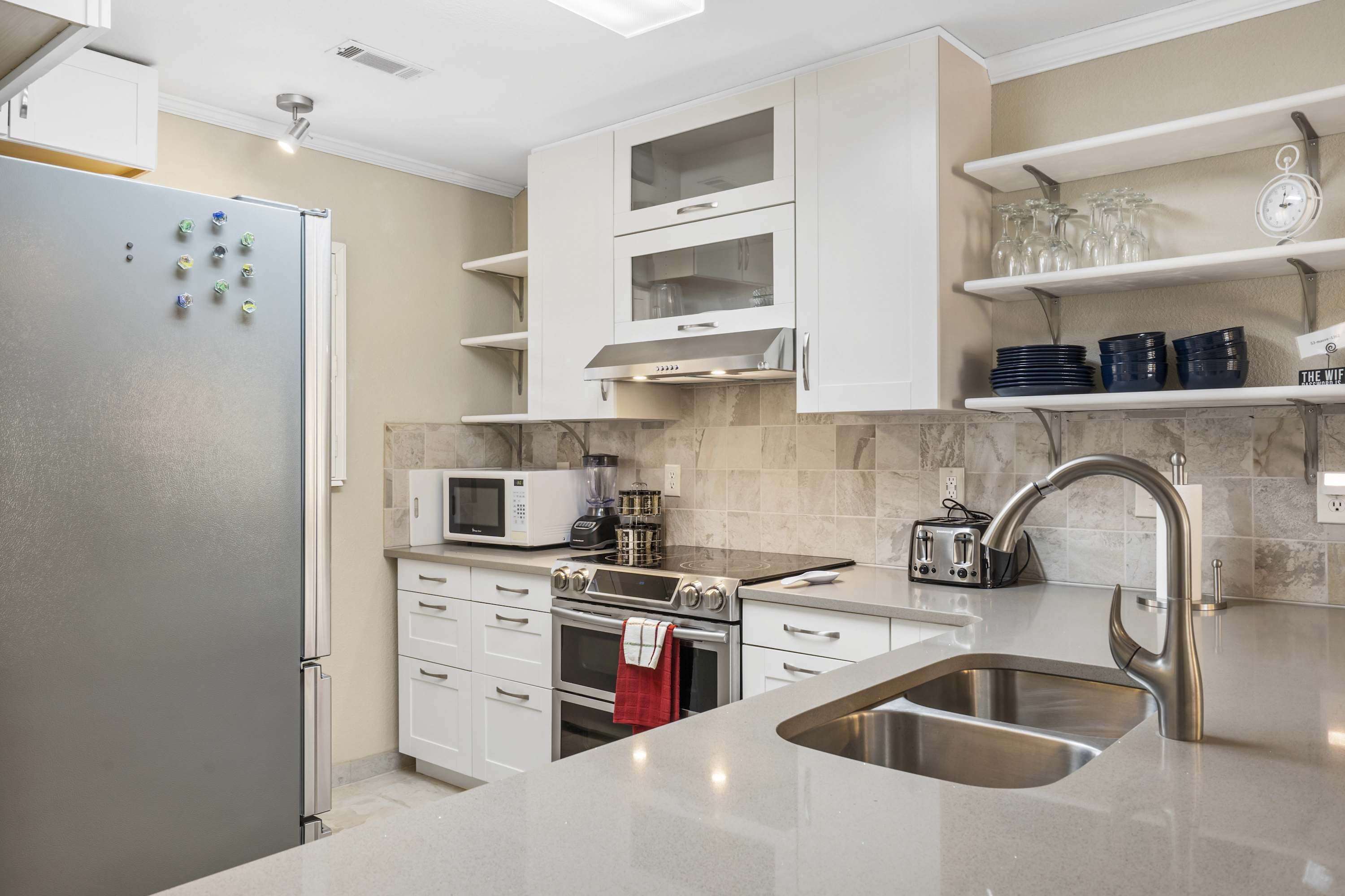 Eine moderne Küche mit Edelstahl-Kühlschrank, Mikrowelle, Backofen, Spüle und weißen Schränken.