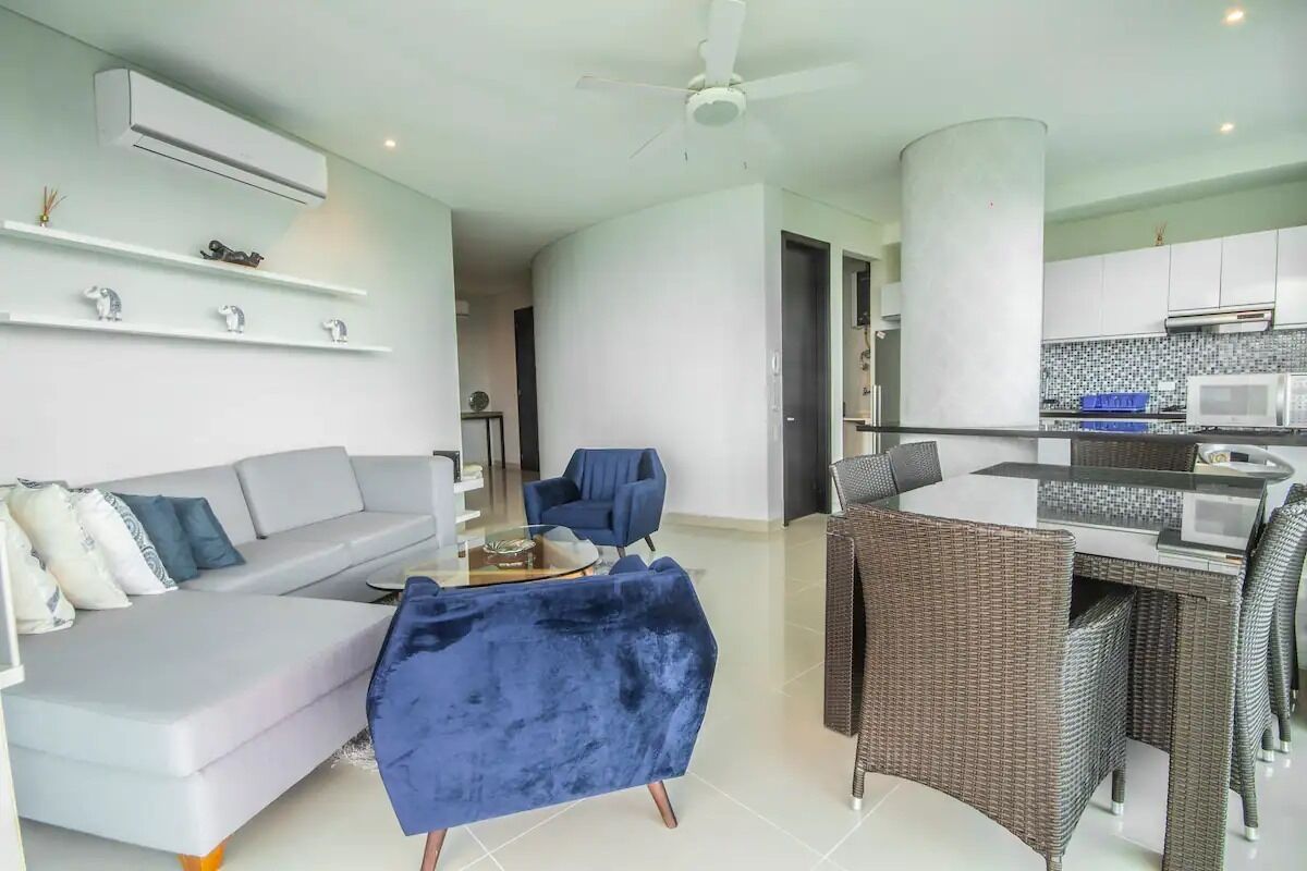A modern living room with a grey sofa, a blue armchair, and a dining area with wicker chairs and a white table.