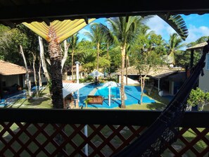 A pool area with a hammock, palm trees, and thatched-roof buildings. - Pousada Água Marinha (Porto Seguro)