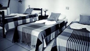A room with two beds, each with a checkered blanket and pillows. There is a framed picture on the wall and a small table with a vase. - Pousada Água Marinha (Porto Seguro)