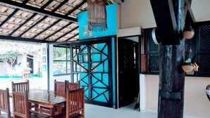 A dining area with wooden chairs and a table, a blue partition wall, and a ceiling with a grid pattern. - Pousada Água Marinha (Porto Seguro)