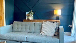 Una sala de estar moderna con un sofá gris, una mesita de madera con una lámpara y una pared de acento azul oscuro.