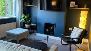 Una sala de estar moderna con un sofá, una mesa de centro redonda de vidrio, un sillón negro, una chimenea y un televisor montado en la pared.
