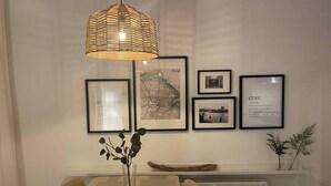 Un comedor con una mesa de madera, sillas, una lámpara colgante de fibras naturales y cuadros en la pared.